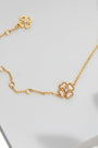 A delicate gold chain bracelet with a small four-leaf clover charm and an adjustable extender chain, styled on a white surface with soft leaf shadows.