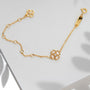 A delicate gold chain bracelet with a small four-leaf clover charm and an adjustable extender chain, styled on a white surface with soft leaf shadows.